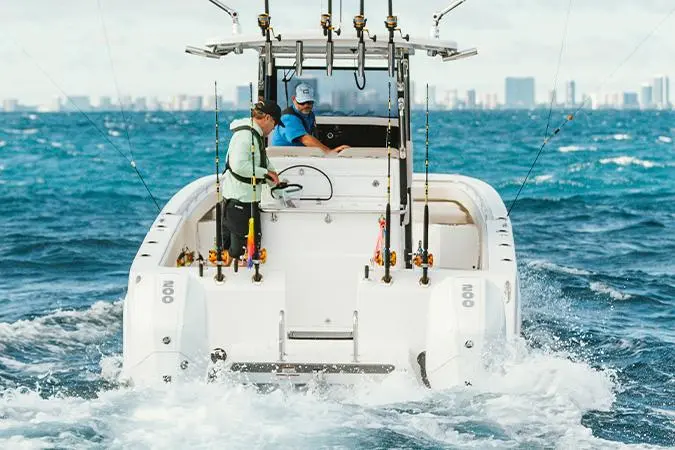 Two fishermen on a boat in deep blue water, with fishing rods and a city skyline visible in the background.